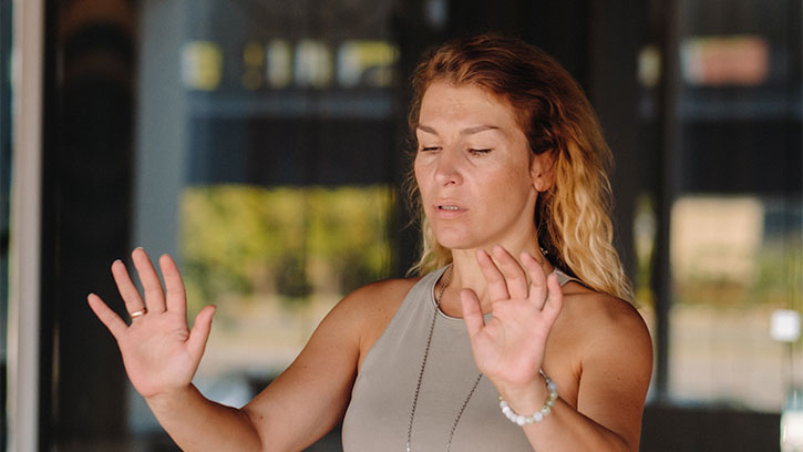 woman with wavy blond hair pointing palms away from her chest in meditation